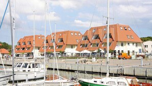 En lystbådehavn med flere både i havnen, en række bygninger med rødt tegltag, og en klar himmel.