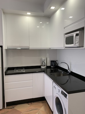 A modern kitchen with white cabinets, a microwave, a coffee maker, and a washing machine.