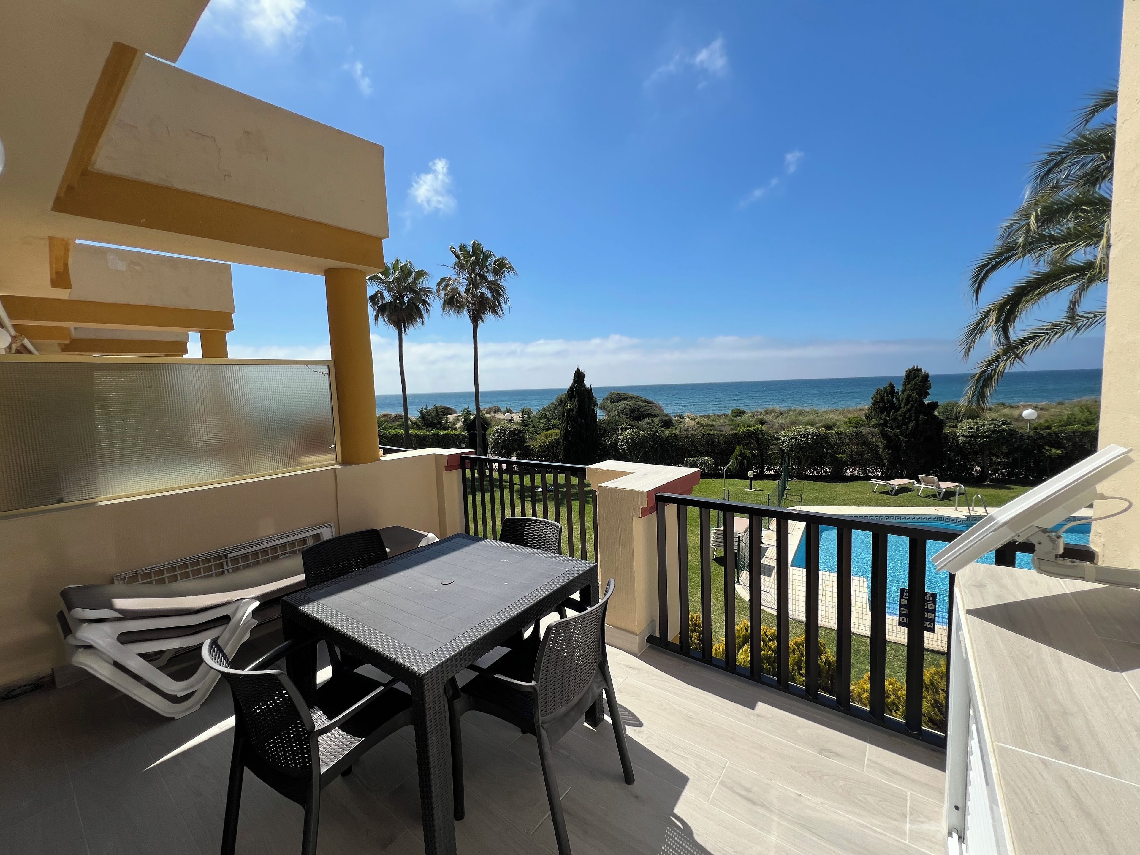 A balcony with a table and chairs, overlooking a pool and the sea.