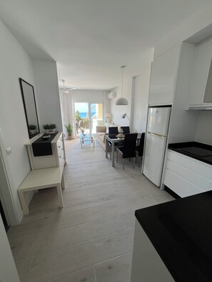 A modern kitchen with white cabinetry, a dining area with a table and chairs, and a view of the ocean through a balcony. - Apartment 815, right on the beach with a view of the ocean (Marbella)