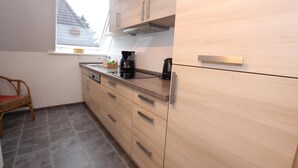 A kitchen with light wood cabinets, a black countertop, and a wicker chair. - Ferienwohnung in Westerland auf Sylt (Westerland)