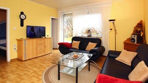Una sala de estar con un sofá, una mesa de centro de vidrio, un televisor sobre un mueble de madera y una lámpara.