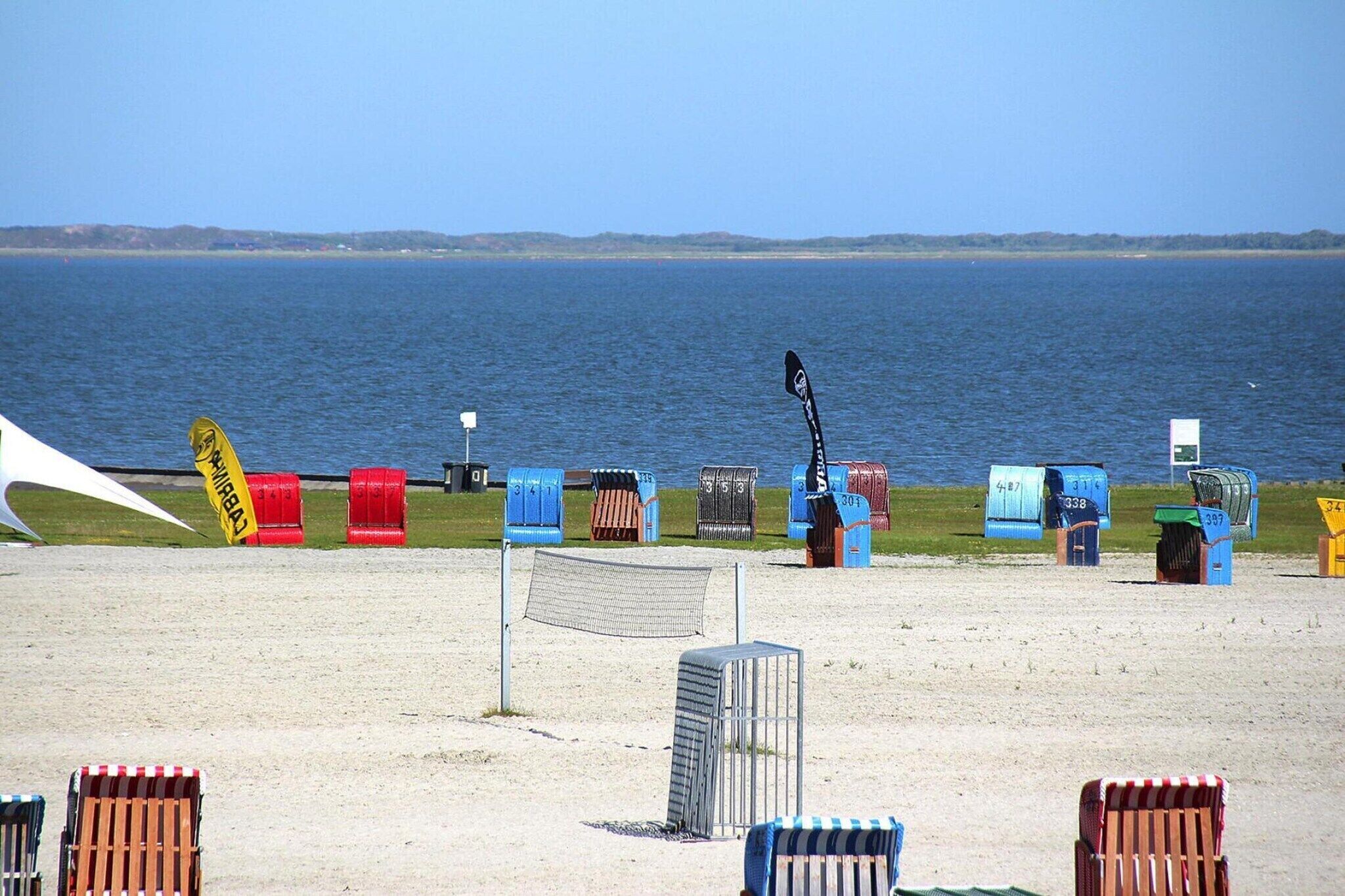 A beach with numbered beach huts and a netted area in the foreground.