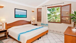 A hotel room with a bed, nightstands, a desk, a window with a view of palm trees, a painting of a sailboat, and a potted plant. - 1 bedroom cozy apartment in Pula (CA) (Pula (CA))