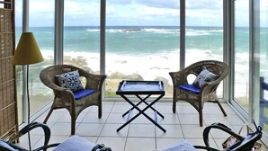 A sunlit room with a view of the ocean, featuring wicker chairs, a small table, and a lamp. - Fisherman's House in Brittany by the Sea (Plouescat)
