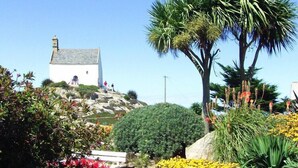 A white building with a grey roof, surrounded by various plants and flowers. - Fisherman's House in Brittany by the Sea (Plouescat)