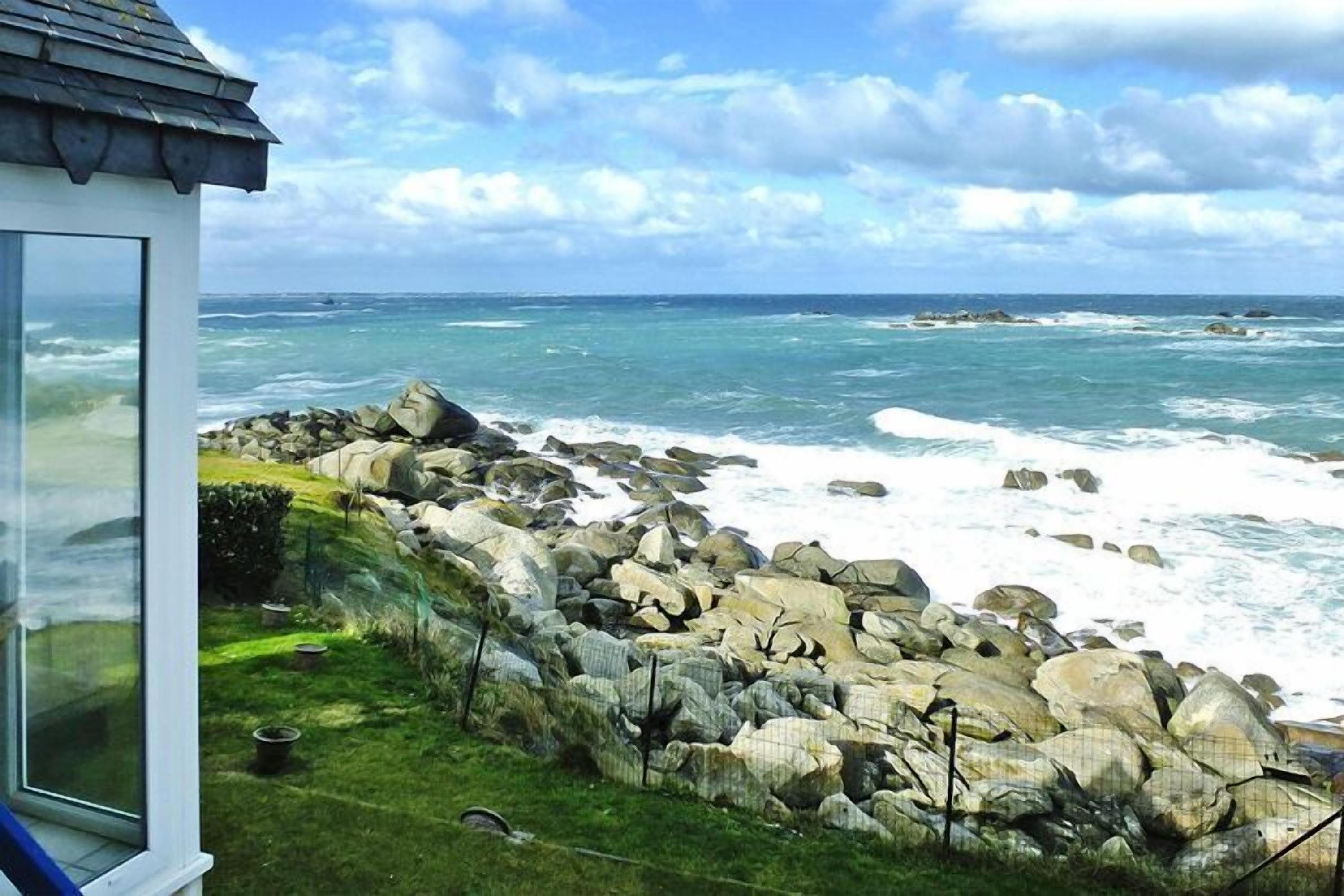 Une vue sur la côte, avec un rivage rocheux, une zone herbeuse et un bâtiment doté d’un toit en pente.