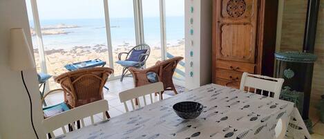 Un coin repas avec une table dressée pour deux personnes, donnant sur une plage.