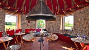 A rustic interior with stone walls, wooden furniture, and a central fire feature. - Holiday Farm by Red River with Indoor Pool (Kindwiller)