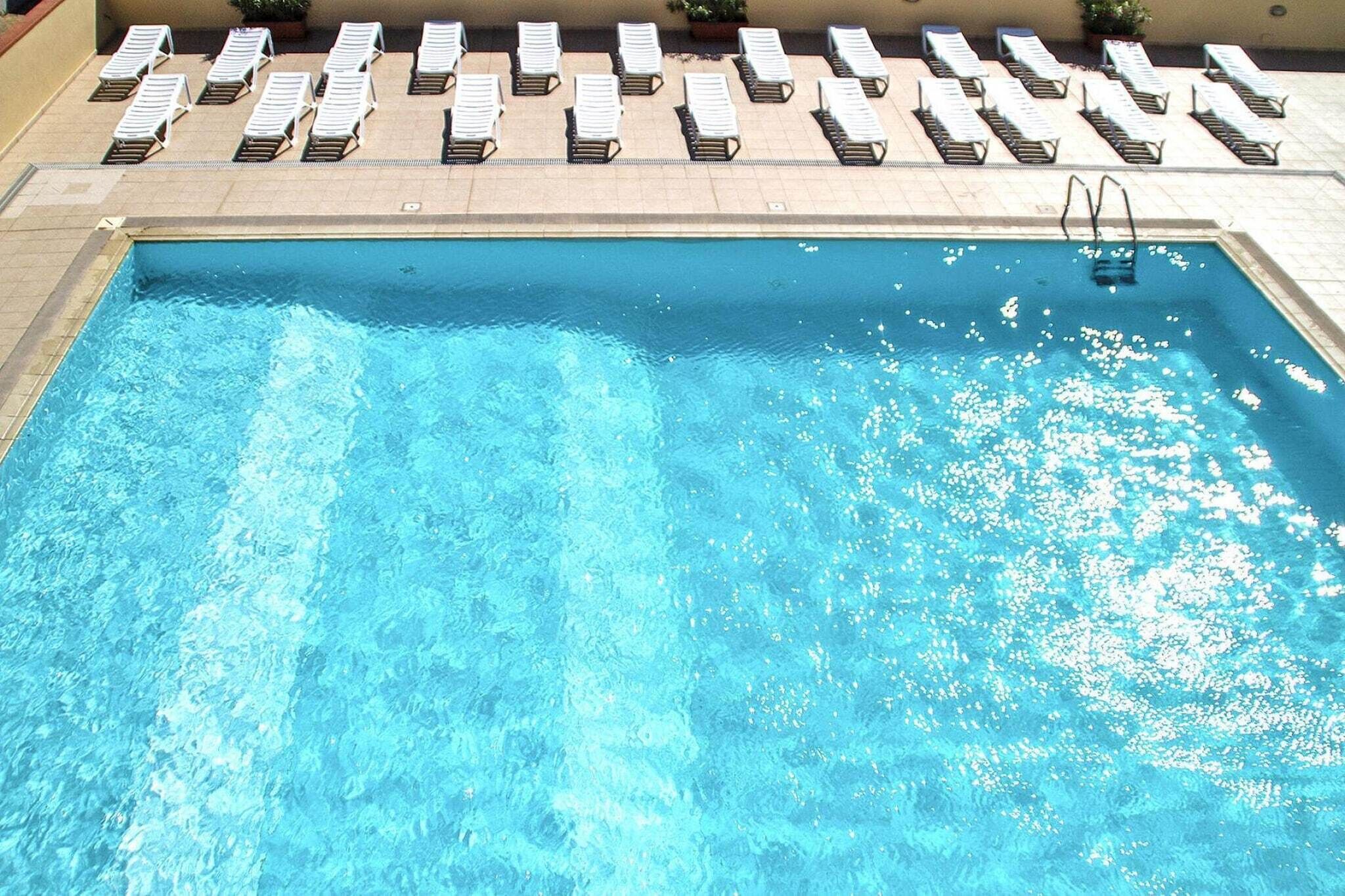 Une piscine rectangulaire à l’eau d’un bleu cristallin, entourée de chaises longues et d’une terrasse carrelée.