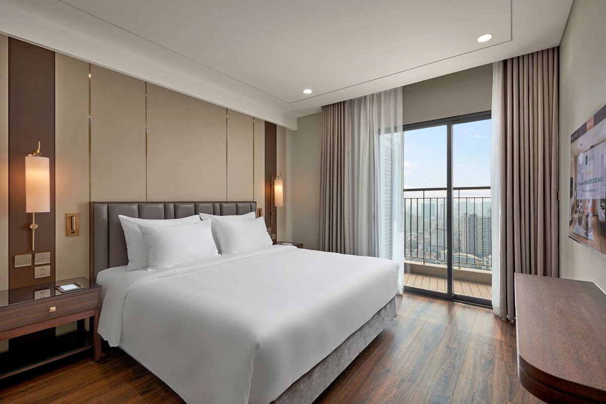 Une chambre d’hôtel moderne dotée d’un grand lit, d’une table de chevet, d’un bureau et d’un balcon offrant une vue sur la ville.