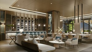 A modern hotel lobby with a seating area, a bar, and a large window offering a view of the outdoors.