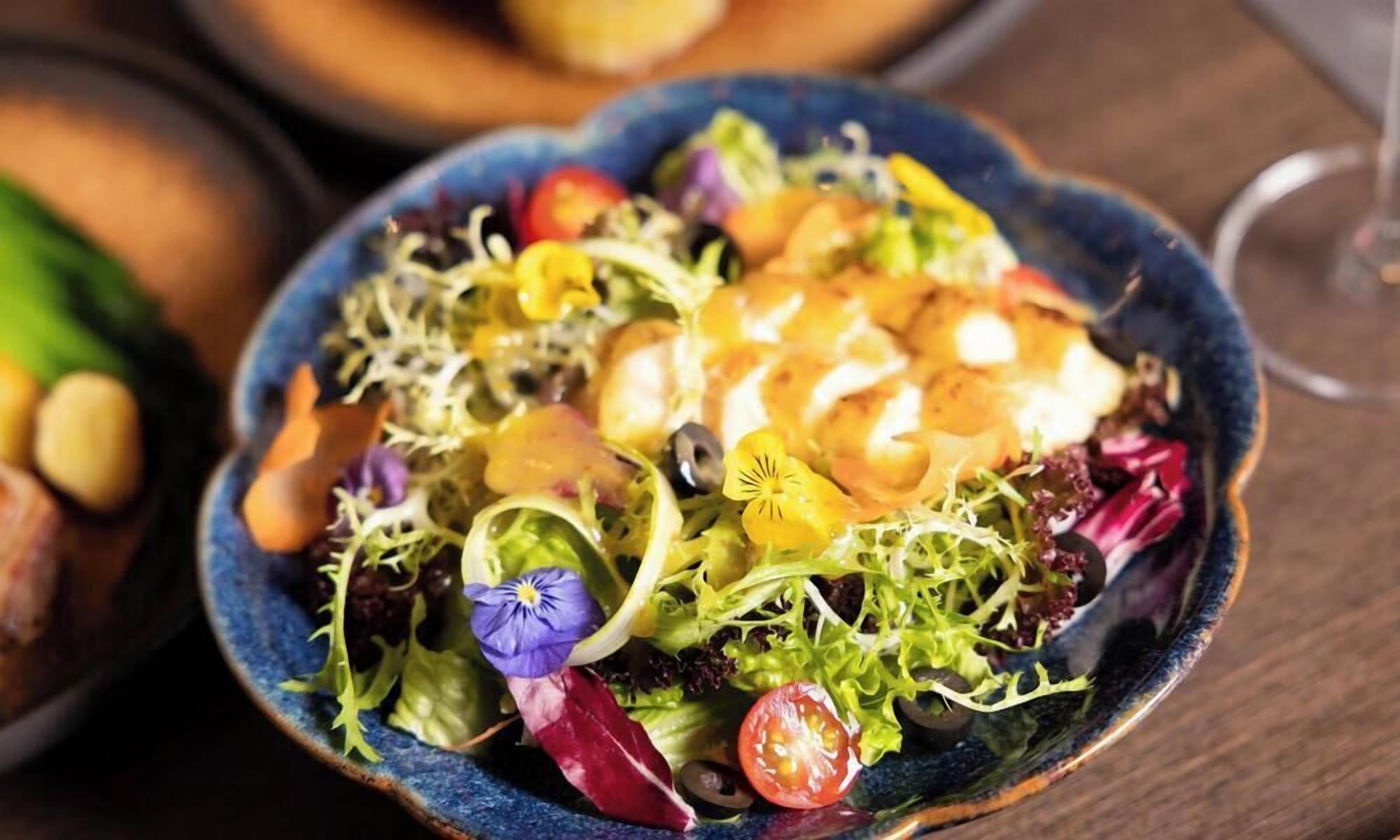 Insalata colorata con diverse verdure e un bicchiere di vino su un tavolo di legno.