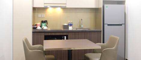 A compact kitchen with a dining table and chairs, a refrigerator, and a coffee maker.