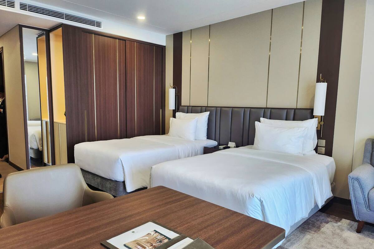 Une chambre d’hôtel avec deux lits, une table en bois, une chaise et un miroir.