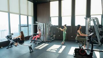 A gym with cardio machines, weightlifting equipment, and large windows offering city views.