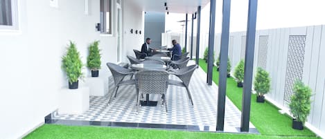 Eine überdachte Terrasse mit Gartenmöbeln, einem Schachbrettmuster-Boden und Topfpflanzen.