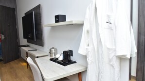 Camera d'albergo con una scrivania in legno, una TV a schermo piatto montata a parete, un bollitore e un accappatoio appeso alla porta.