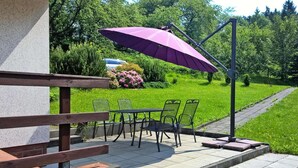 An outdoor patio with a table and chairs, a purple umbrella, and a garden in the background. - Ferienhaus, Steinbach-Hallenberg (Steinbach-Hallenberg)