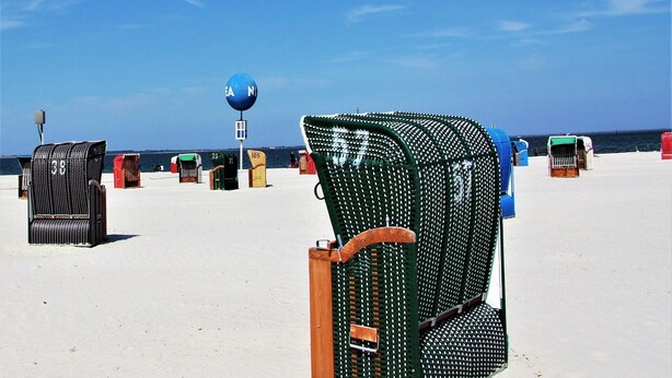 A beach with several beach chairs and a blue sign in the background. - Ferienhaus, Dornumersiel (Dornumersiel)