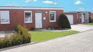 A red brick building with numbered doors, a small lawn, and a paved driveway. - Ferienhaus, Dornumersiel (Dornumersiel)
