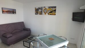 A small living area with a sofa, a glass-top table with chairs, and a TV mounted on the wall. - Beautiful renovated apartment for 4 with private parking in Roses (Roses)