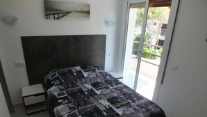 A bedroom with a large bed, a headboard, a small bedside table, and a view of the outdoors through a sliding glass door. - Beautiful renovated apartment for 4 with private parking in Roses (Roses)