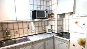A kitchen with white cabinets, a microwave, a coffee maker, and a sink. - Cozy 2-Bed Apartment with Terrace & AC, 800m from Beach – Alberes 42, Empuriabrava (Castelló d'Empúries)