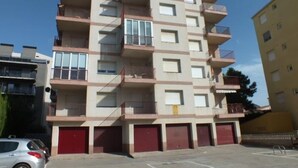 A multi-story residential building with balconies, a parking area, and red garage doors.