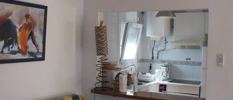 Un salon comprenant un canapé, un tableau, un miroir, ainsi qu’un coin cuisine avec un évier et une bouilloire.