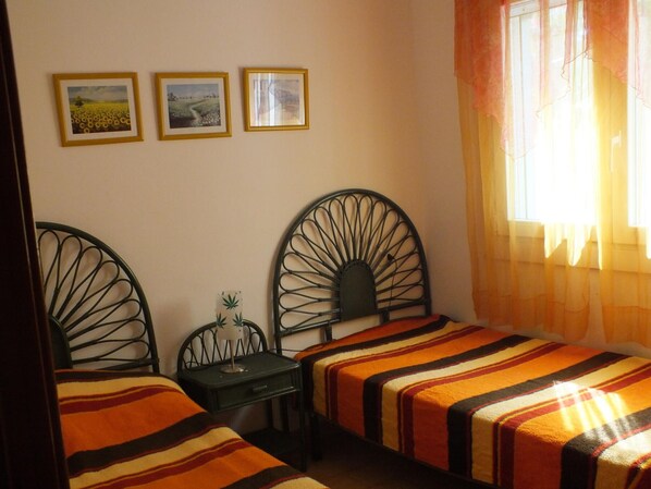 Quarto com duas camas, uma mesa de cabeceira e três quadros na parede.