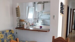 A compact living space with a kitchenette, a sofa, two stools, and a dining table with a floral tablecloth.