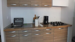 Une cuisine de taille réduite, dotée de meubles en bois, d’un évier en acier inoxydable, d’une machine à café et d’une cuisinière à gaz.