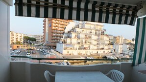 Un balcon avec une table et des chaises, donnant sur une marina où sont amarrés des bateaux, et sur un immeuble à plusieurs étages également doté de balcons.