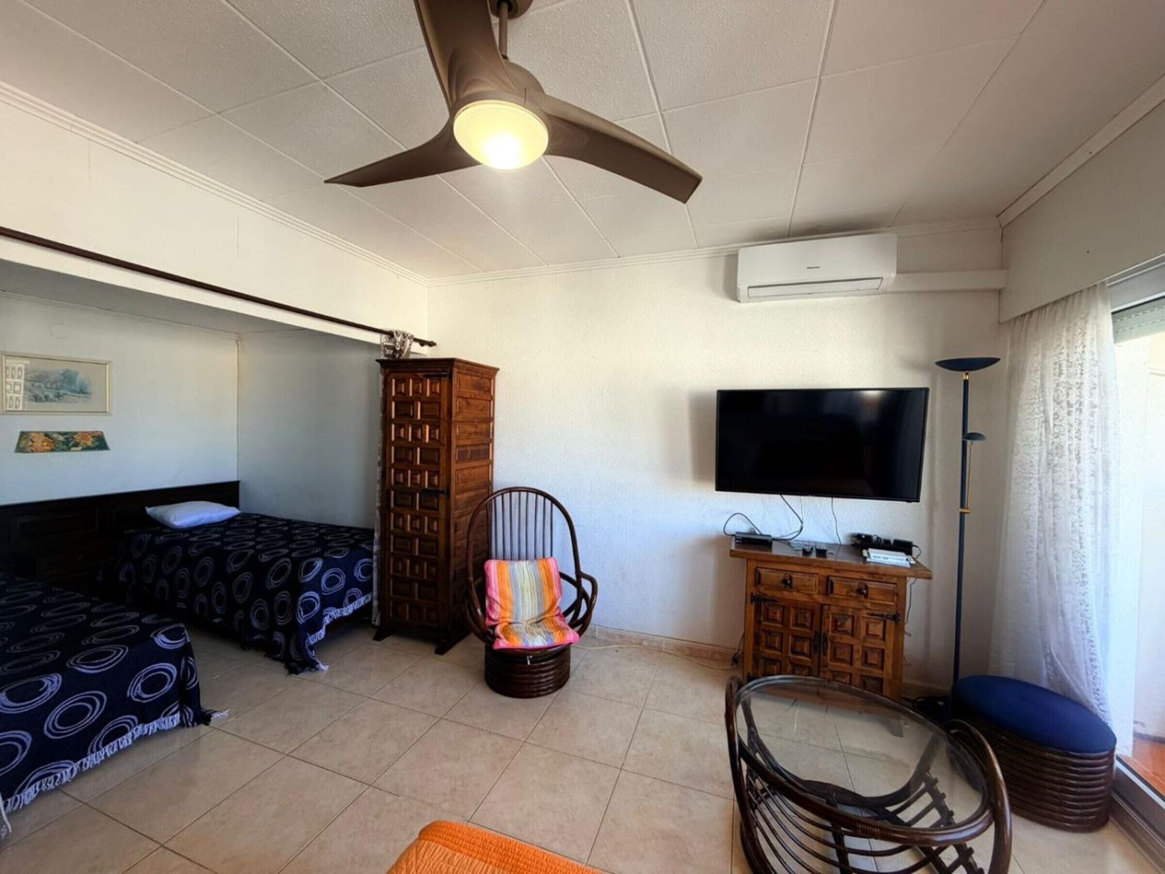 Una habitación de hotel con cama, una silla, televisión y ventilador de techo.