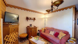 A cozy living room with a television, wooden furniture, a patterned sofa, and a ceiling fan.
