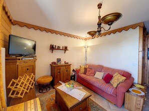Una sala de estar acogedora con televisor, muebles de madera, un sofá estampado y un ventilador de techo.