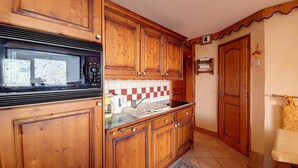 A compact kitchen with wooden cabinets, a microwave, a stove, and a tiled backsplash.