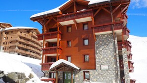 A multi-story wooden building with balconies and a stone facade, surrounded by snow.