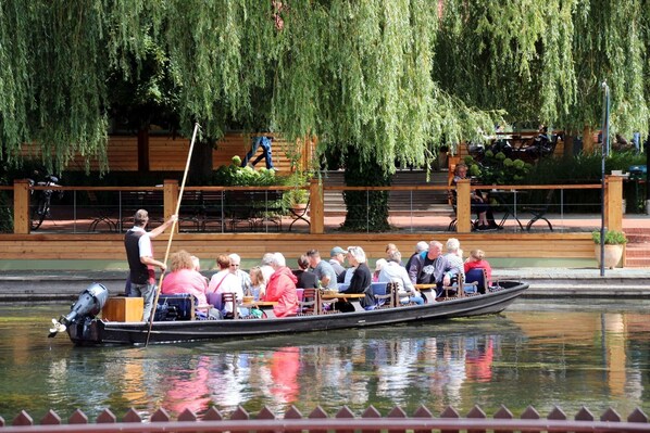 A rowboat with passengers, a wooden deck, and a weeping willow tree in the background.