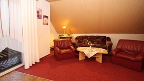 A cozy living room with a red carpet, leather armchairs, a patterned sofa, and a small table with a floral tablecloth.