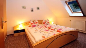 A bedroom with a wooden bed, floral bedding, a nightstand with a lamp, a small drawer, and a skylight.