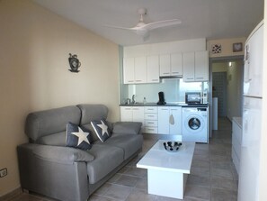 A compact living space with a sofa, a coffee table, a washing machine, and a kitchenette.