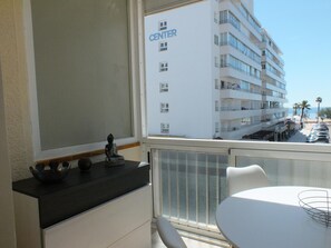 Ein Balkon mit Blick auf ein mehrstöckiges Gebäude mit der Aufschrift 'CENTER', einem Tisch mit Stühlen und einer Buddha-Statue auf der Fensterbank.