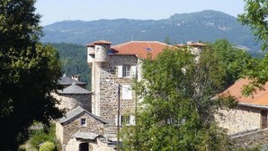 A stone building with a red-tiled roof, surrounded by greenery and hills in the background. - Rural Pool Retreat in the Hills (Retournac)