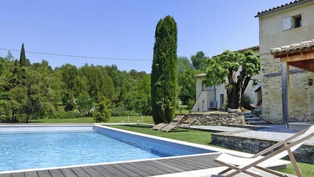 A swimming pool with a wooden deck, lounge chairs, and a stone wall. - Relaxing Home Near Pool in Malaucène (Malaucène)