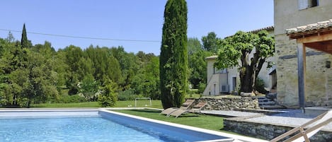 Une piscine avec une terrasse en bois, des chaises longues et un mur en pierre.