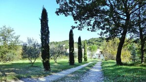 A gravel path leading through a garden with tall trees and a building in the background. - Relaxing Home Near Pool in Malaucène (Malaucène)