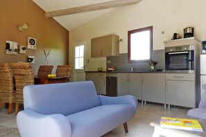 A modern kitchen with a dining area, featuring a sofa, wicker chairs, and a table with a fruit bowl.