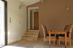 A dining area with a table and four wicker chairs, a staircase leading to an upper level, and a door with a glass panel.